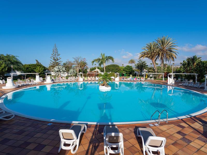 Piscine extérieure ronde ensoleillée avec chaises longues et palmiers autour.