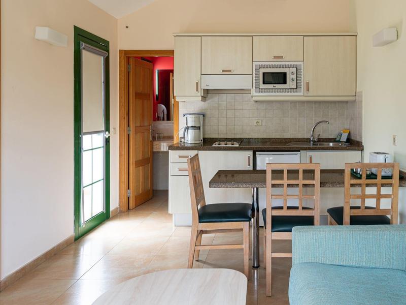 Cuisine et salle à manger confortables avec chaises en bois, canapé bleu et porte verte dans une pièce lumineuse.