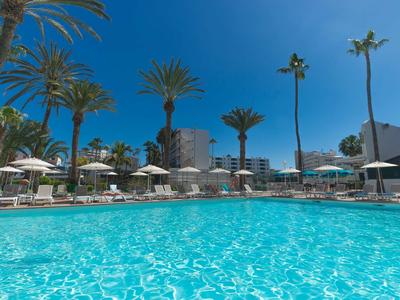 Großer Pool in einem Hotel mit Palmen und Sonnenschirmen unter klarem Himmel.