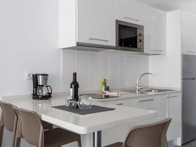 Coin cuisine moderne avec plan de travail blanc, micro-ondes, cafetière et espace repas.