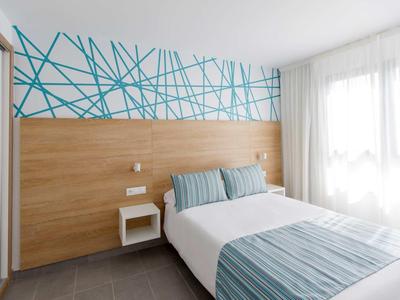 Chambre d'hôtel lumineuse avec tête de lit en bois, design mural moderne et grande fenêtre.