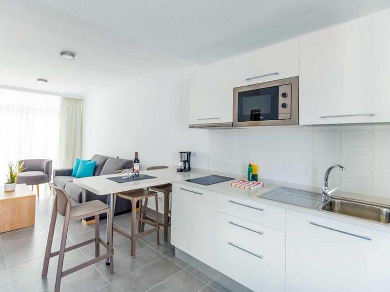 Coin cuisine moderne et lumineux avec armoires blanches, tabourets de bar et coin repas en arrière-plan.