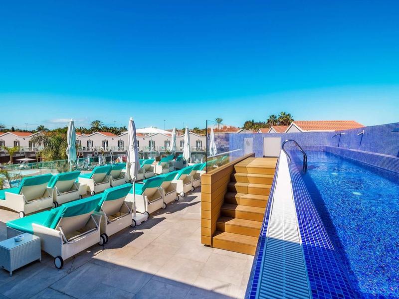 Nowoczesny basen z niebieskimi leżakami i schodami obok wody