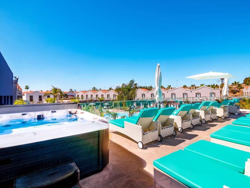 Strefa basenowa z leżakami i jacuzzi pod błękitnym niebem w hotelu.