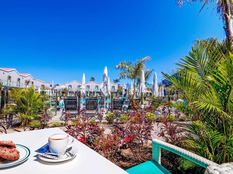 Widok z tarasu z kawą i ciastkami na rośliny i budynki hotelowe pod czystym niebieskim niebem.