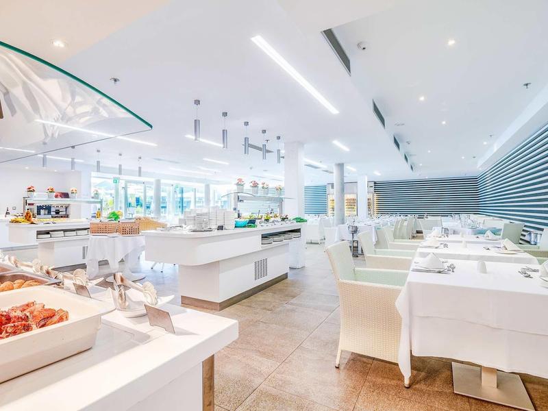 Jasna, nowoczesna restauracja hotelowa z elegancko nakrytymi stołami i bufetem.