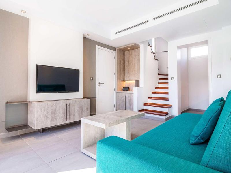 Nowoczesny salon z turkusową sofą, telewizorem na ścianie i drewnianymi schodami w tle.