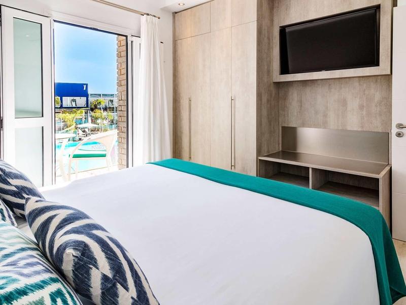 Nowoczesny pokój hotelowy z łóżkiem podwójnym, telewizorem i balkonem z widokiem na basen.