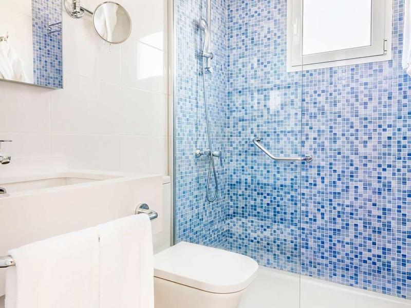 Nowoczesna łazienka z niebieskimi mozaikowymi płytkami, toaletą i umywalką z ręcznikiem.