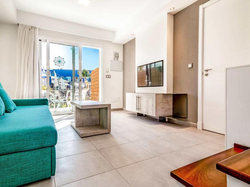 Jasny pokój hotelowy z turkusową sofą, telewizorem i balkonem z widokiem na miasto.