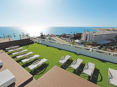 Lettini su una terrazza sul tetto con vista sul mare e sugli edifici dell'hotel.