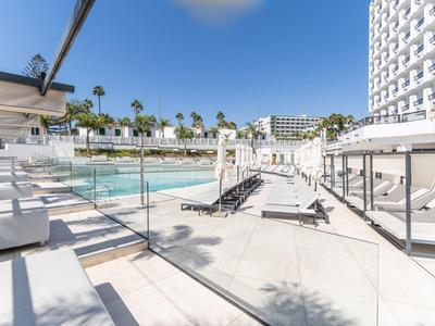 Espace piscine extérieur moderne d'hôtel avec transats et palmiers sous un ciel bleu.