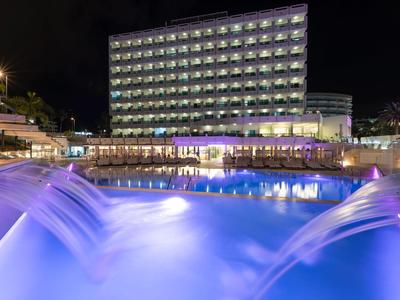 Edificio moderno di un hotel con piscina illuminata e cascate di notte