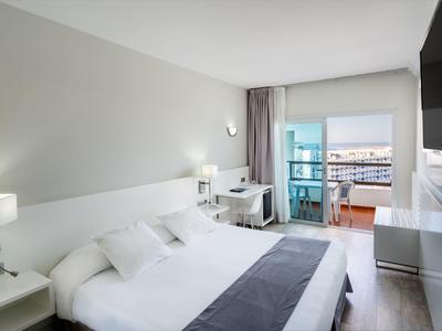 Chambre d'hôtel moderne avec grand lit, bureau et balcon avec vue sur la mer.