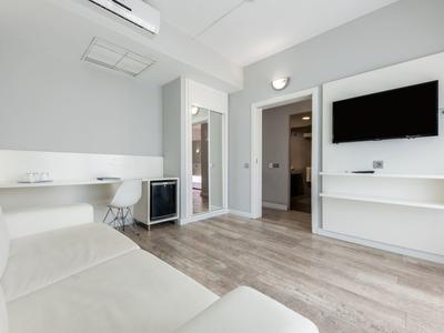 Chambre d'hôtel moderne avec canapé, bureau, TV et sol en bois.