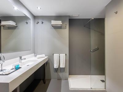 Salle de bain d'hôtel moderne avec douche, deux lavabos et grands miroirs.