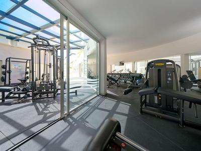 Palestra moderna con macchine per pesi e grande parete di vetro che si affaccia su un'area esterna coperta.