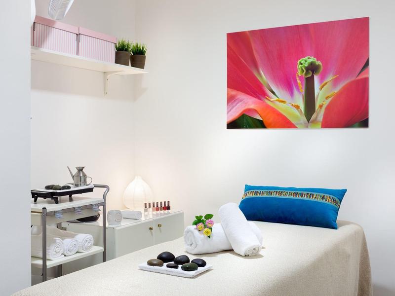 Salle de soin lumineuse avec table de massage, coussin coloré et décoration murale florale en gros plan.