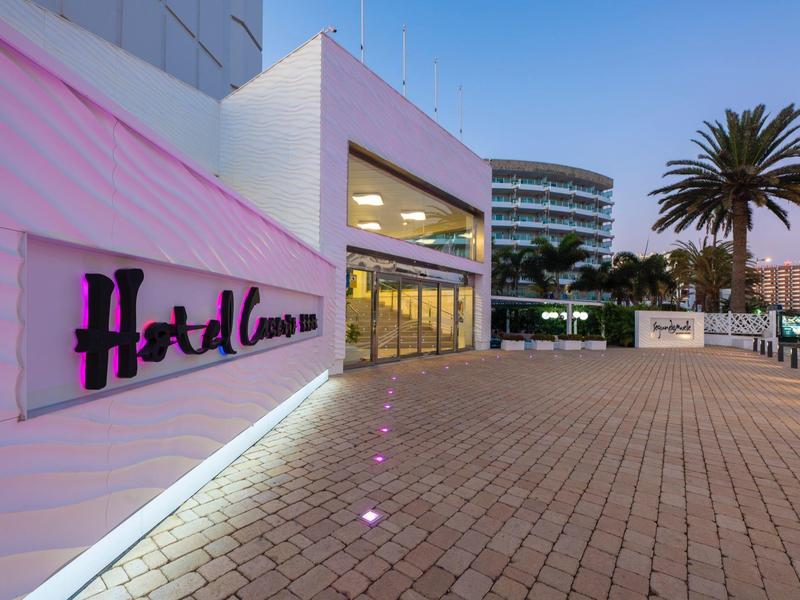 Entrée moderne d'hôtel avec allée pavée et palmiers au crépuscule.