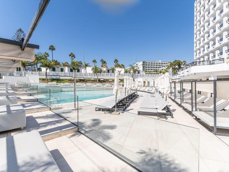 Espace piscine extérieur moderne d'hôtel avec transats et palmiers sous un ciel bleu.