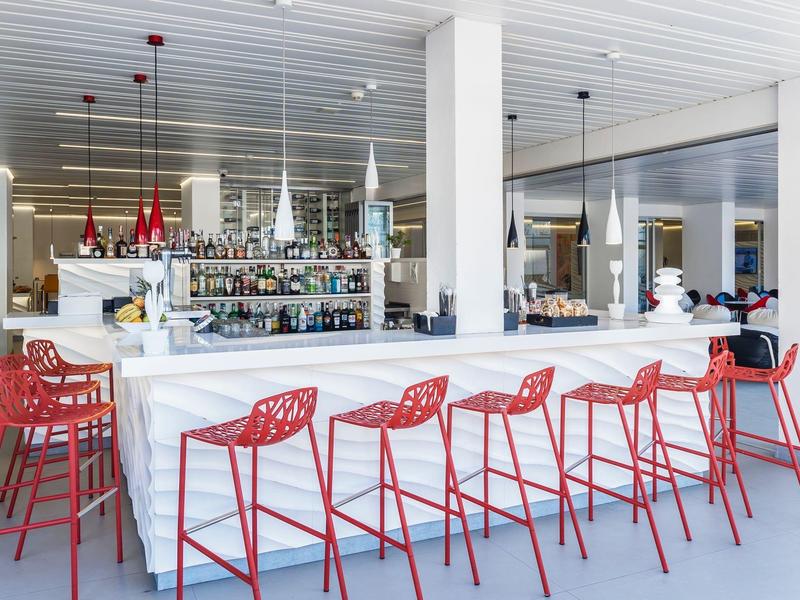 Bar moderne avec surfaces blanches et tabourets rouges dans une pièce lumineuse.