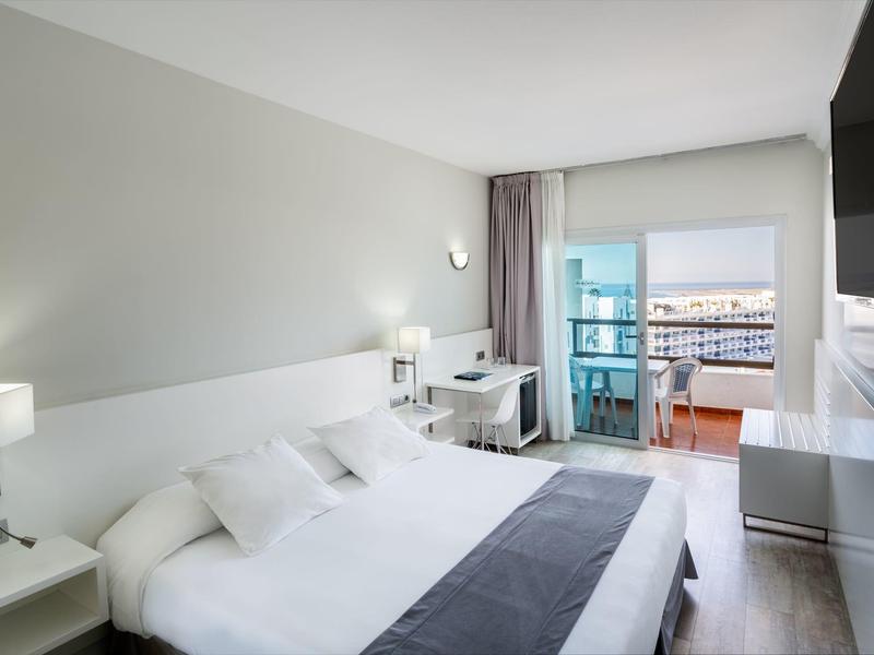 Chambre d'hôtel moderne avec grand lit, bureau et balcon avec vue sur la mer.