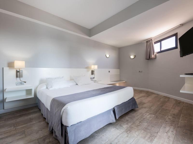 Chambre d'hôtel lumineuse avec lit double, éclairage mural et télévision murale.