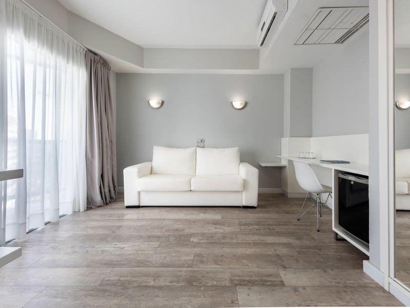 Chambre d'hôtel lumineuse et moderne avec canapé, grande fenêtre et design minimaliste.