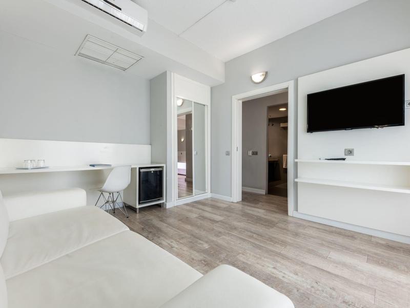 Chambre d'hôtel moderne avec canapé, bureau, TV et sol en bois.