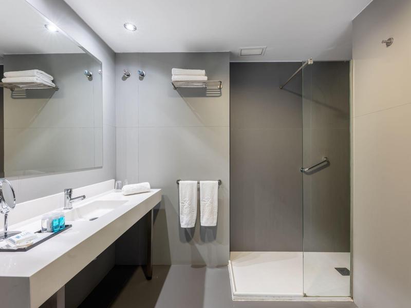 Salle de bain d'hôtel moderne avec douche, deux lavabos et grands miroirs.