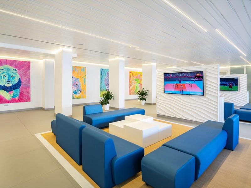 Salon moderne d'hôtel avec sièges bleus, table blanche et œuvres d'art colorées aux murs.