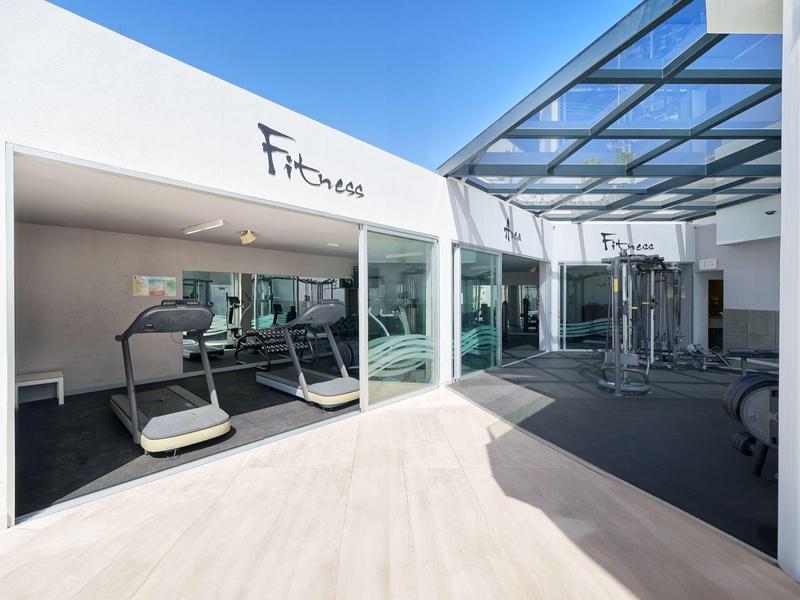 Espace fitness moderne avec tapis de course et machines à câble sous un toit en verre.