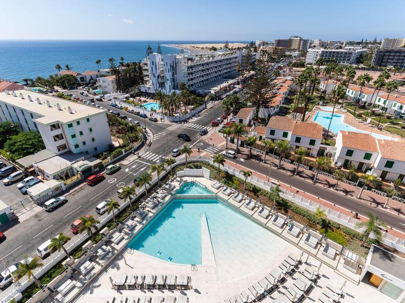 Vue d'un hôtel avec une grande piscine entourée de chaises longues près de la côte.