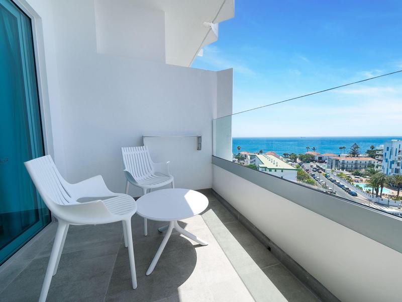 Balcon avec deux chaises blanches et une petite table avec vue sur la mer par ciel clair.