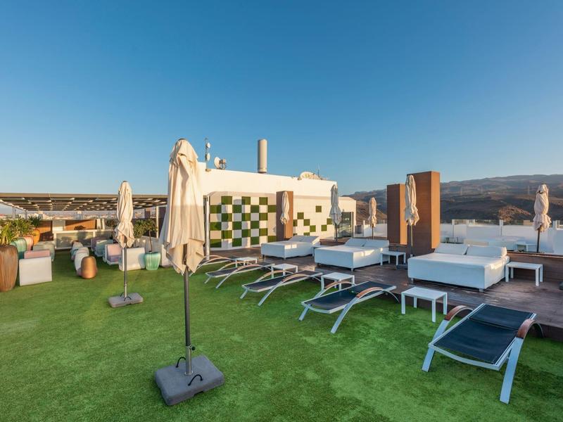 Terrasse sur le toit avec transats, parasols et espace lounge sous ciel clair.