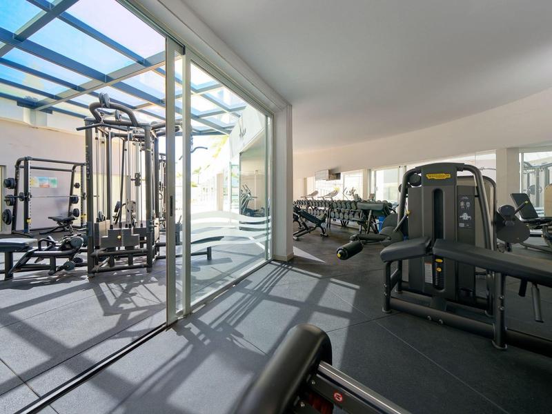 Salle de sport moderne avec appareils de musculation, haltères et grande fenêtre laissant passer la lumière naturelle.