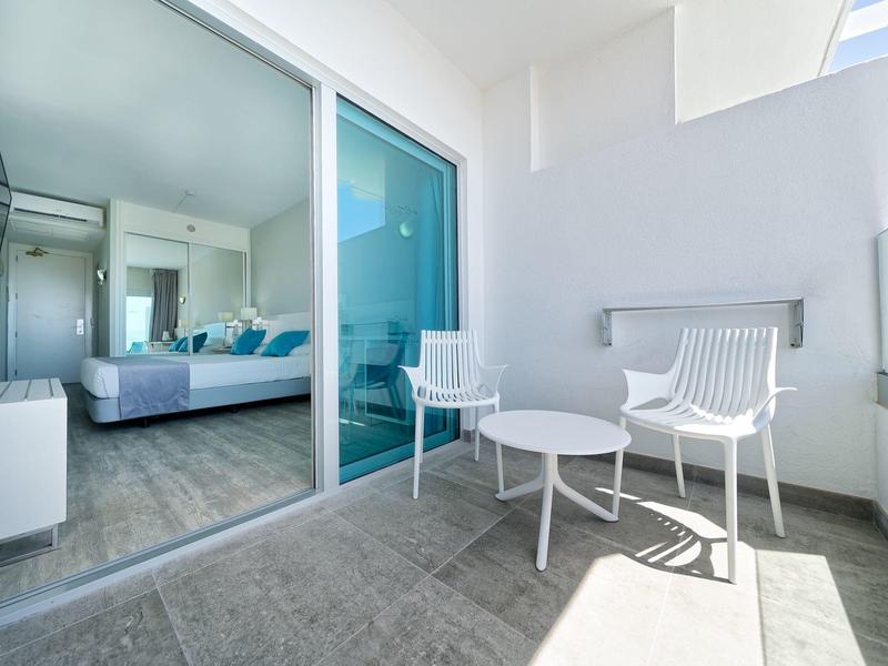 Balcon moderne avec deux chaises blanches et une petite table ronde à côté de la porte coulissante menant à la chambre.