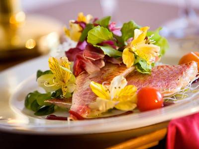 Elegante voorgerecht met visfilet, eetbare bloemen en kleine tomaten op een wit bord.
