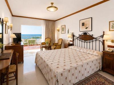 Lichte hotelkamer met tweepersoonsbed, rustiek meubilair en balkon met zeezicht.