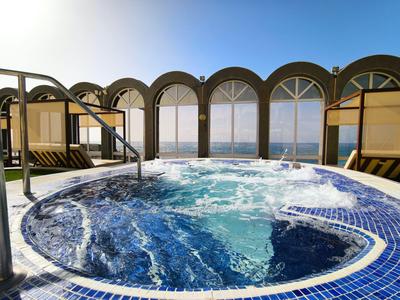 Ronde jacuzzi op een terras met panoramische ramen, uitzicht op zee bij heldere lucht.