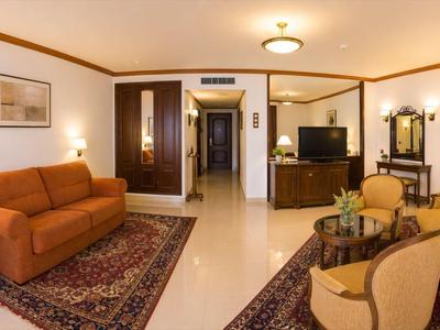 Gezellige hotelkamer met bank, fauteuils, tapijten en tv in warm licht.