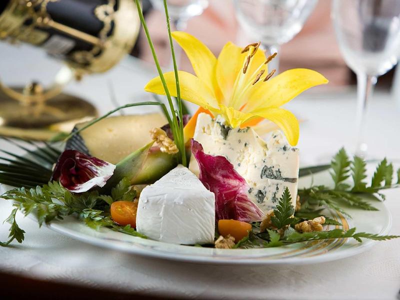 Elegant appetizer with cheese, edible flowers, and leaves arranged on a white plate.