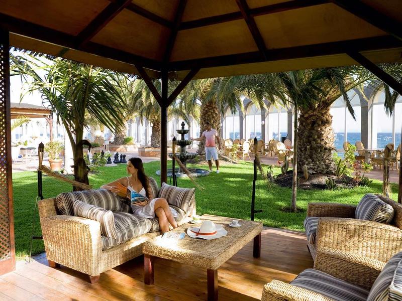 Cozy lounge under a pavilion with wicker furniture overlooking palm trees and lawn.