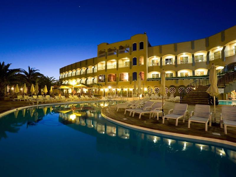 Illuminated hotel with outdoor pool and lounge chairs at night under clear sky.