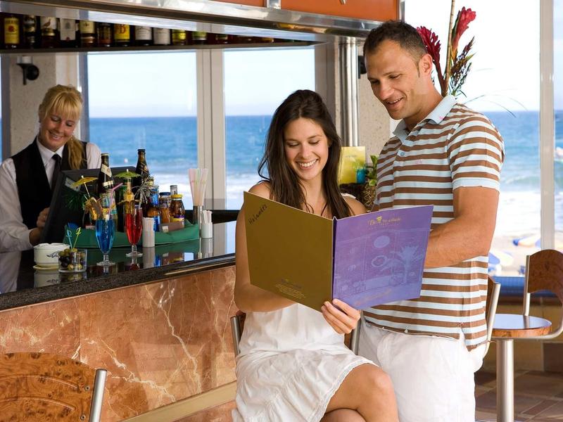 Couple reading a menu together at a bar with a sea view.
