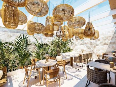 Heller Frühstücksraum mit Holz- und Rattanmöbeln, vielen Pflanzen und Korblampen unter Glasdach.