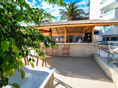Bar al aire libre con techo de paja y taburetes junto a edificio blanco
