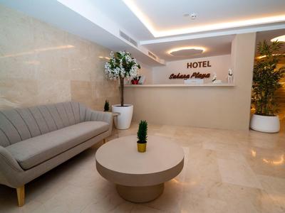 Elegante vestíbulo de hotel con mesa redonda, sofá y plantas en un ambiente moderno.