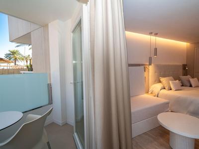 Nowoczesny pokój hotelowy z łóżkiem podwójnym, jasną zasłoną i miejscem do siedzenia przy oknie.