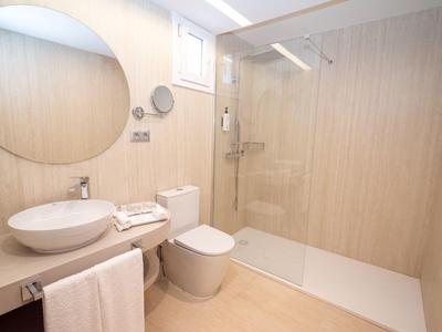 Nowoczesna łazienka z prysznicem bez progów, okrągłym lustrem i białą armaturą.